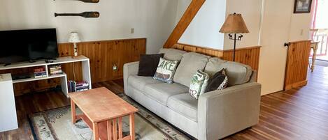 A living room with a sofa, a coffee table, a TV, and a wooden ceiling.