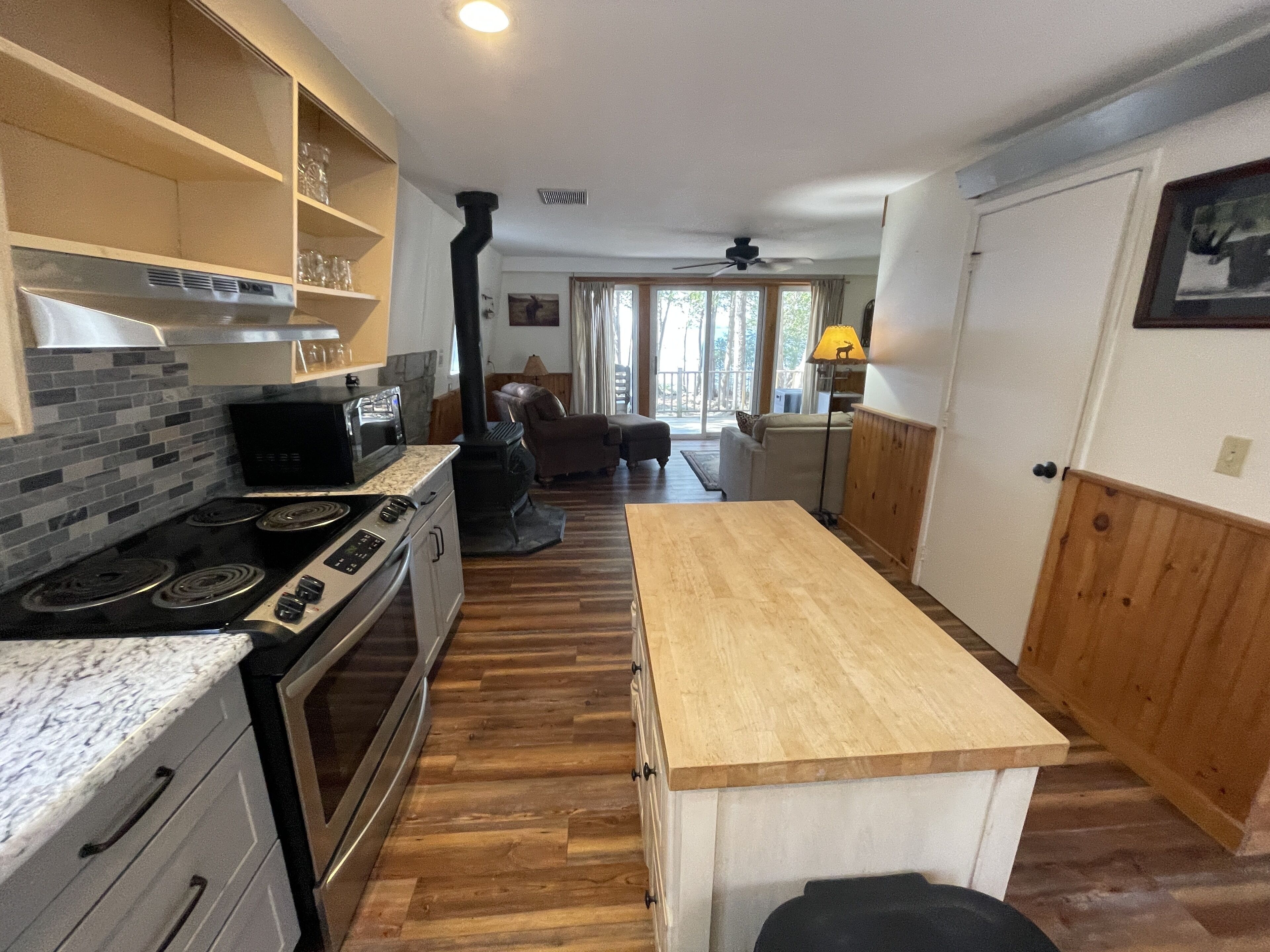 A kitchen with a stove, oven, and microwave, wooden flooring, and a view to the living area.