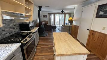 A kitchen with a stove, oven, and microwave, wooden flooring, and a view to the living area.
