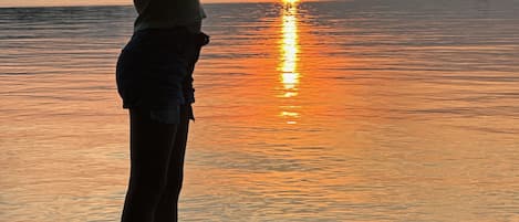 Una persona de pie sobre una roca junto al agua al atardecer.