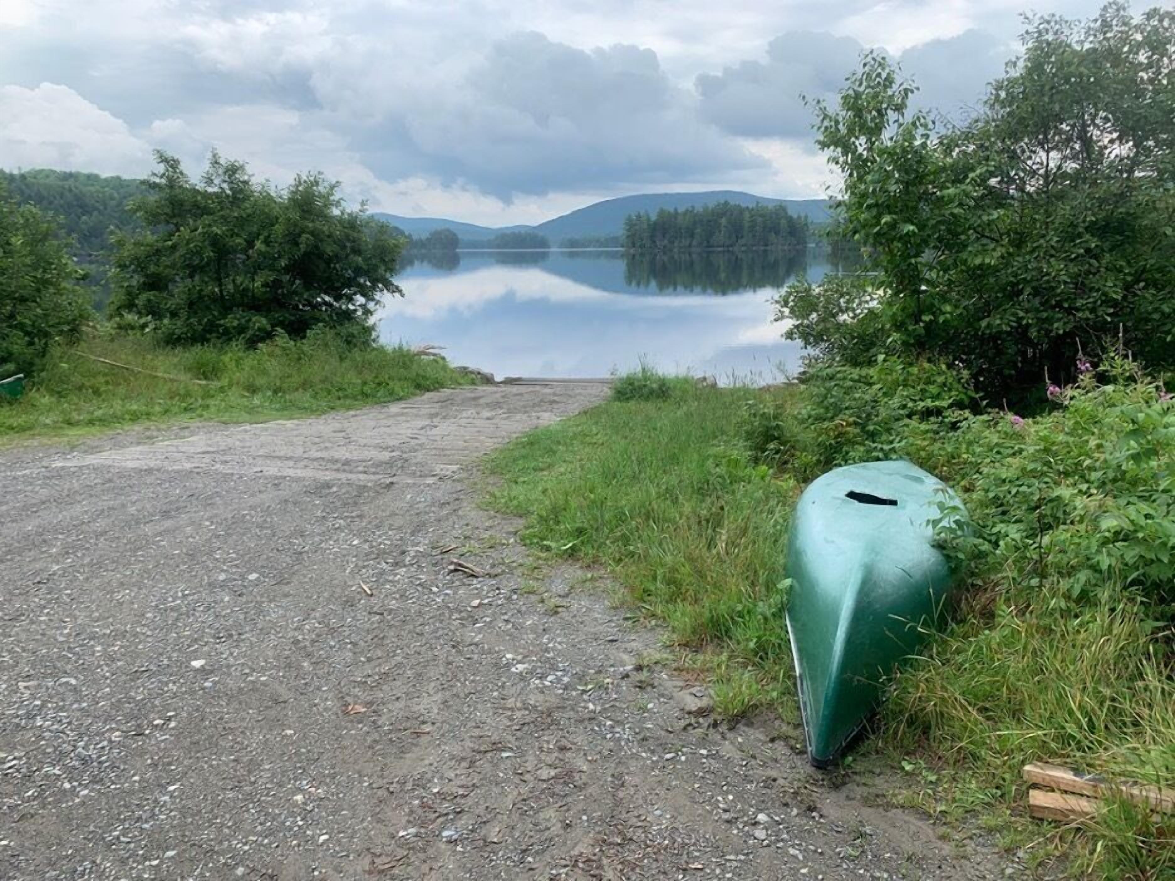 A gravel path leading to a calm lake surrounded by dense greenery and hills.