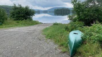 Un sentier de gravier mène à un lac paisible, bordé d’une végétation luxuriante et entouré de collines.