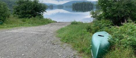 A gravel path leading to a calm lake surrounded by dense greenery and hills.