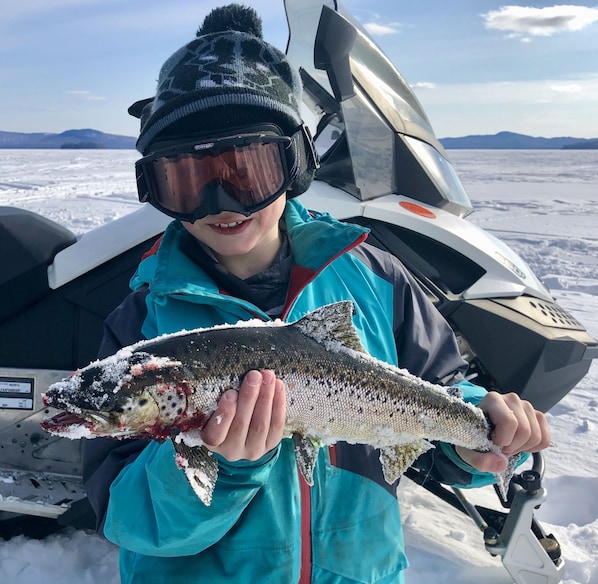A person holding a fish in a snowy outdoor setting with a vehicle in the background.