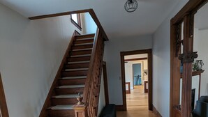 Eine Holztreppe mit einer Bank am Fuß, die zu einem Flur mit Holzböden und Blick auf einen Essbereich führt.