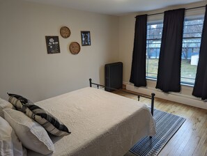 Un dormitorio con cama, radiador, ventana con cortinas y adornos en la pared.