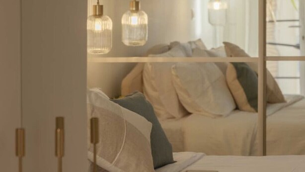 A bedroom with a large mirror reflecting a bed with pillows and a hanging light fixture. - Urban Athéna Apartment,Pangrati (Athina)