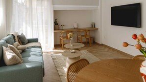 A modern living room with a sofa, a dining table, and chairs. There is a flat-screen TV mounted on the wall. - Urban Athéna Apartment,Pangrati (Athina)
