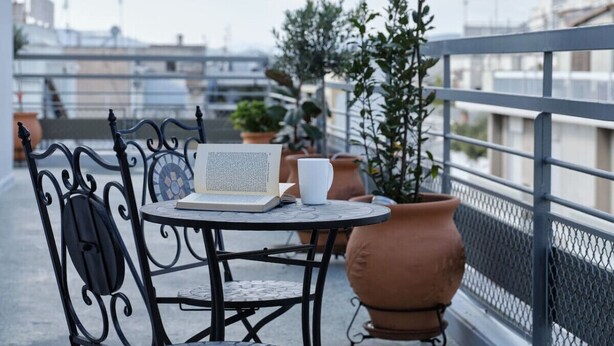 Un balcon avec une table, des chaises, un ordinateur portable, un livre, une tasse et des plantes en pot.