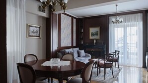 Un coin repas avec une table ronde, des chaises et un lustre. On aperçoit un canapé et une cheminée au fond.