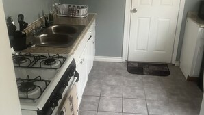 A kitchen with a stove, sink, and cabinets. There is a door and a mat at the entrance.