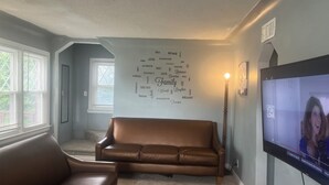 A living room with a brown leather sofa, a flat-screen TV, and a wall with word art.
