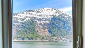 A window with a view of a snow-capped mountain, a forested area, and a body of water.