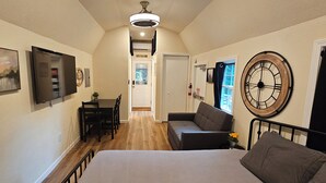 A compact room with a bed, a sofa, a dining table with chairs, a TV, and a clock on the wall.