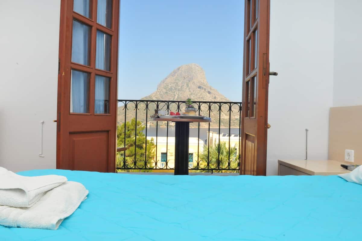 A room with a bed, a table with a plant, and a view of a mountain.