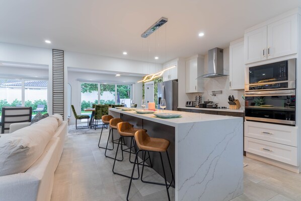 A modern kitchen with white cabinets, a marble island, and a built-in oven. - • 1-Min Walk to Private Beach • Free Heated Pool • Tiki & Putting Green • Games (Pompano Beach)