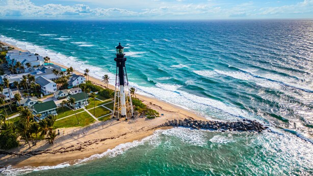 Ein Luftbild einer Küstenregion mit einem Leuchtturm, Strandhäusern und einer felsigen Küstenlinie.