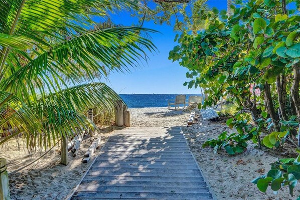 Un sentier en bois mène à une plage où se trouvent des chaises et un panneau.