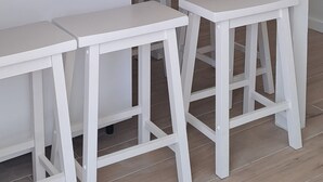 A white kitchen with a white countertop, two white stools, and a ceiling fan.