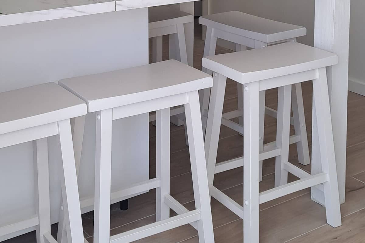 Une cuisine blanche avec un plan de travail blanc, deux tabourets blancs et un ventilateur de plafond.