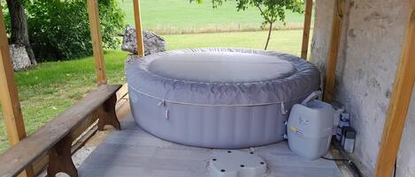 A hot tub in a covered outdoor area with a wooden bench and a view of a green field.