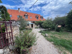 A house with a red-tiled roof, a stone wall, and a gravel path leading to the entrance.