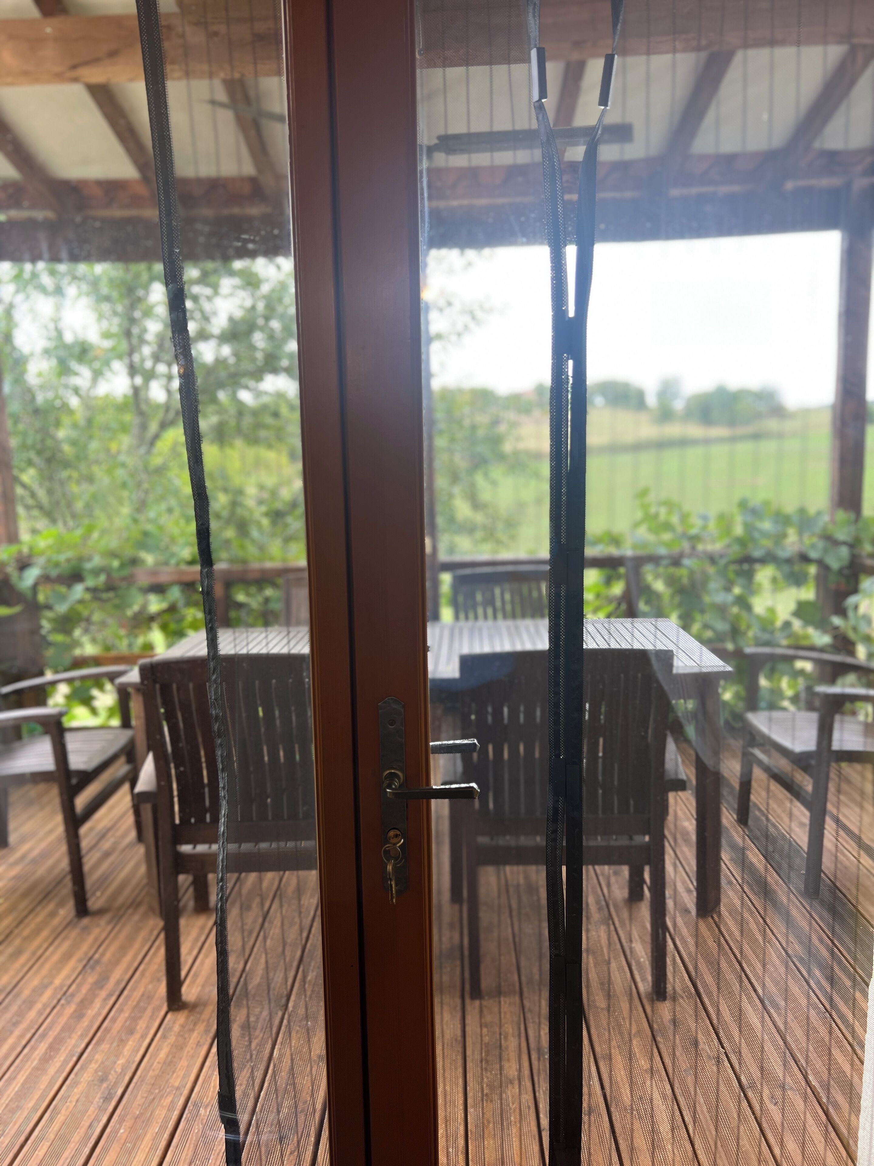 Una terraza de madera con mobiliario exterior, una reja metálica y vistas al follaje.