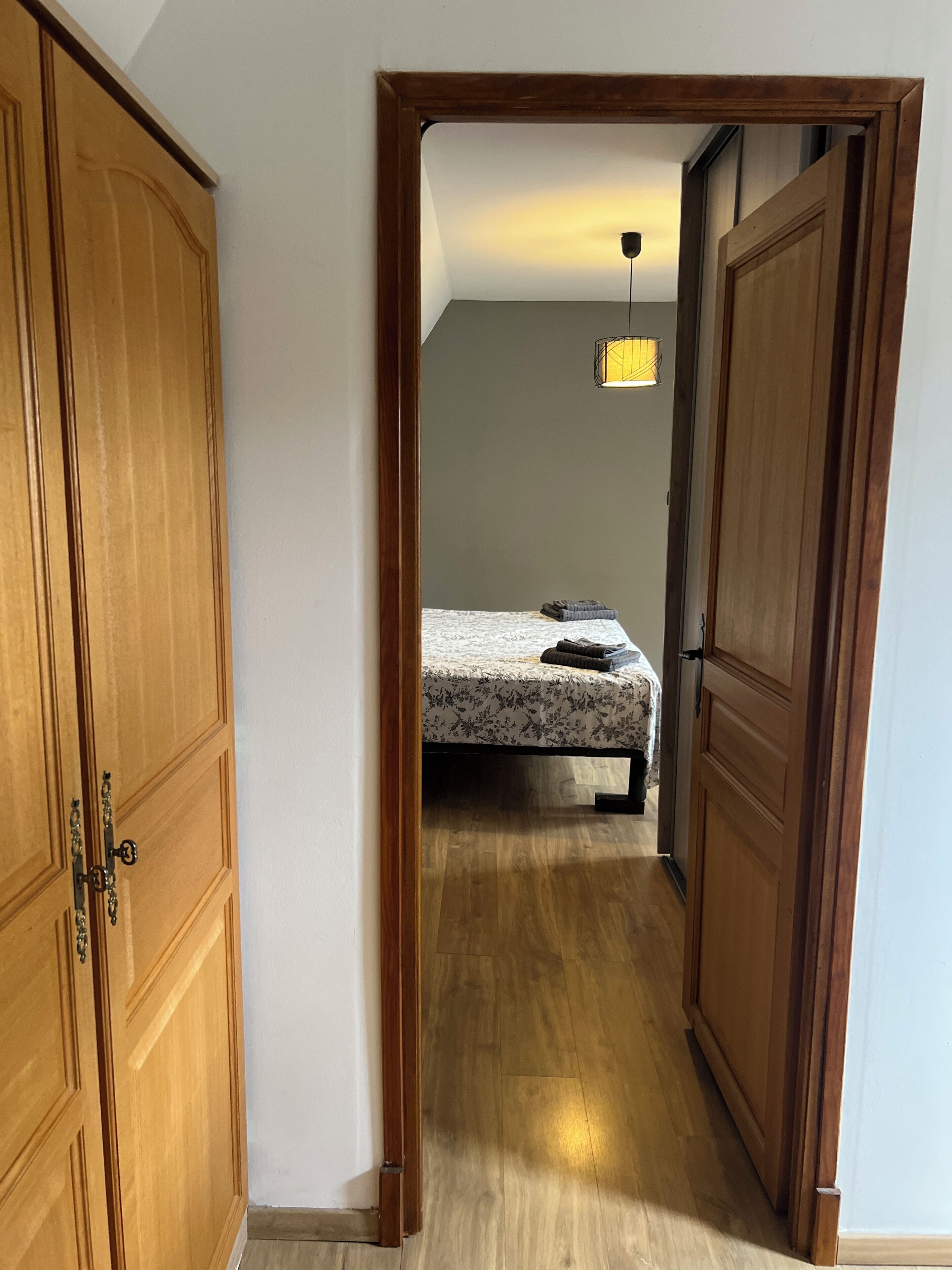 Un pasillo que conduce a un dormitorio con una cama, un armario de madera y una lámpara colgante.