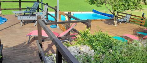 A wooden deck with lounge chairs and a pool area.