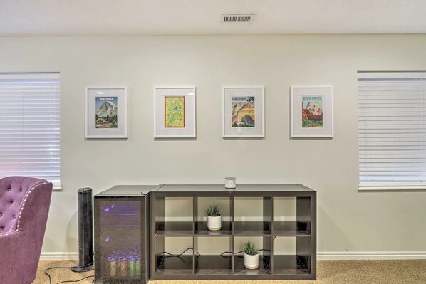 Une pièce avec un fauteuil violet, une vitrine en verre contenant des plantes et quatre œuvres d’art encadrées accrochées au mur.