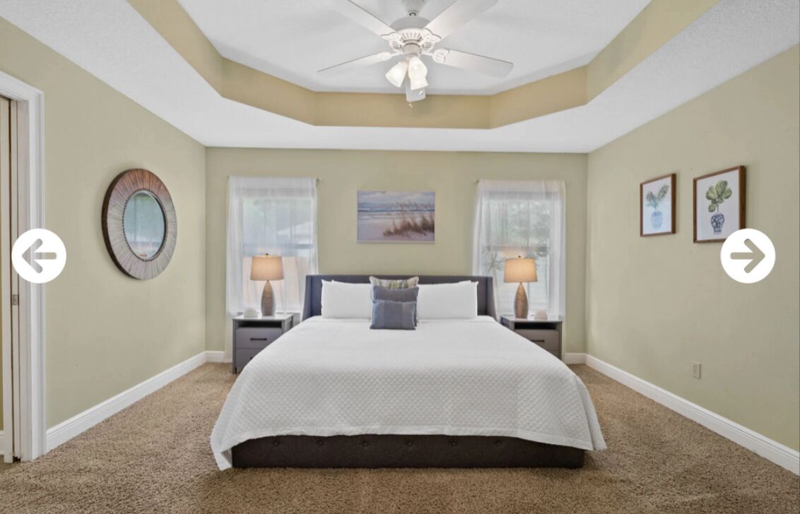 A bedroom with a large bed, two bedside tables with lamps, a ceiling fan, and a wall-mounted mirror.