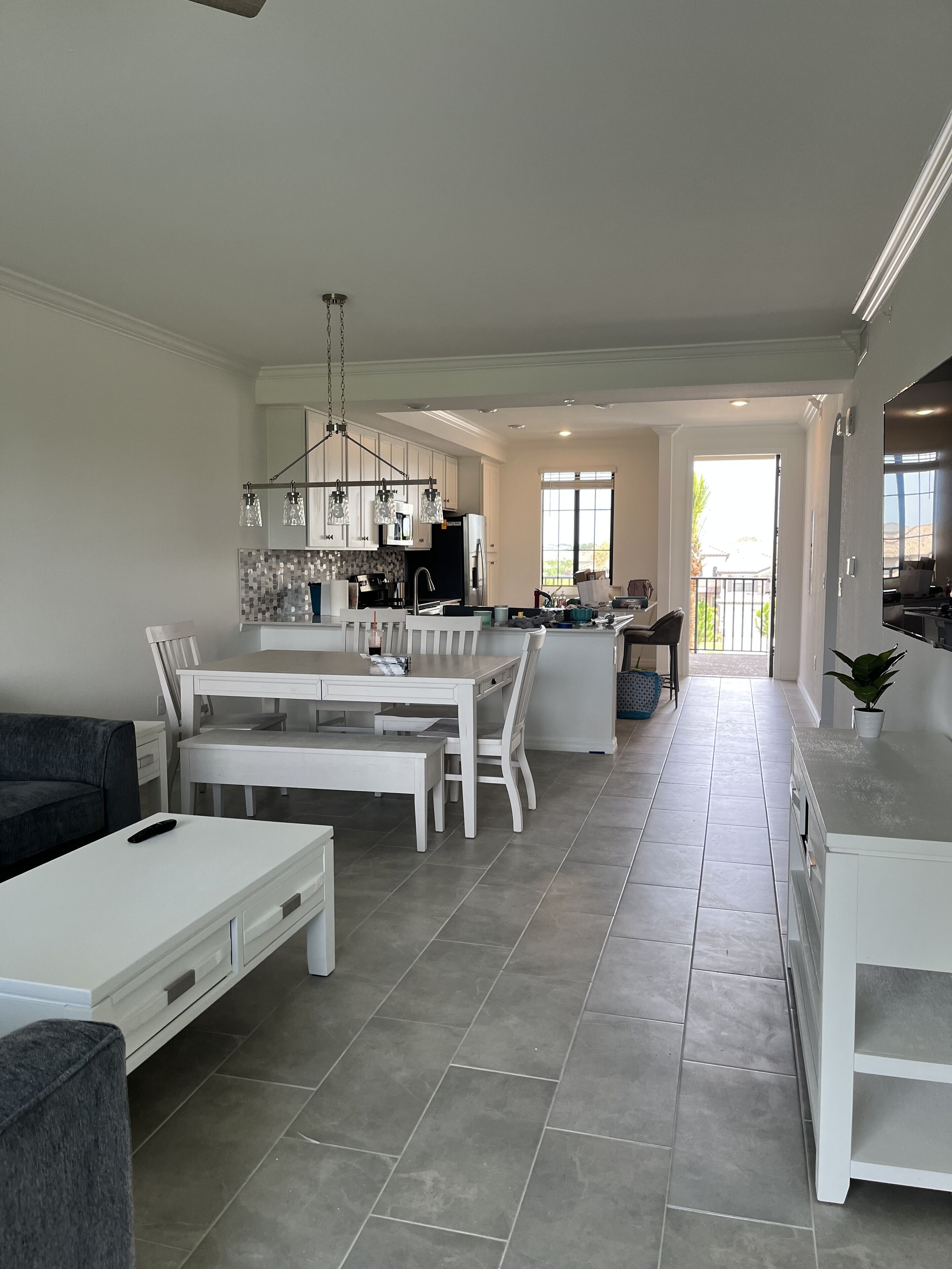 A spacious kitchen with modern appliances, a dining area with a white table and chairs, and a view of the outside through large windows.