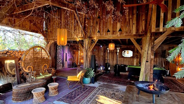 A rustic wooden interior with exposed beams, a fireplace, and a variety of seating and decorative items.