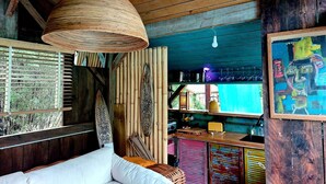 A rustic room with a wooden ceiling, a white sofa, a woven hanging light fixture, and a colorful abstract painting.