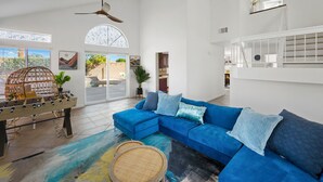 Uma sala de estar ampla com um sofá seccional azul, uma mesa de pebolim e uma grande janela com vista para o exterior.