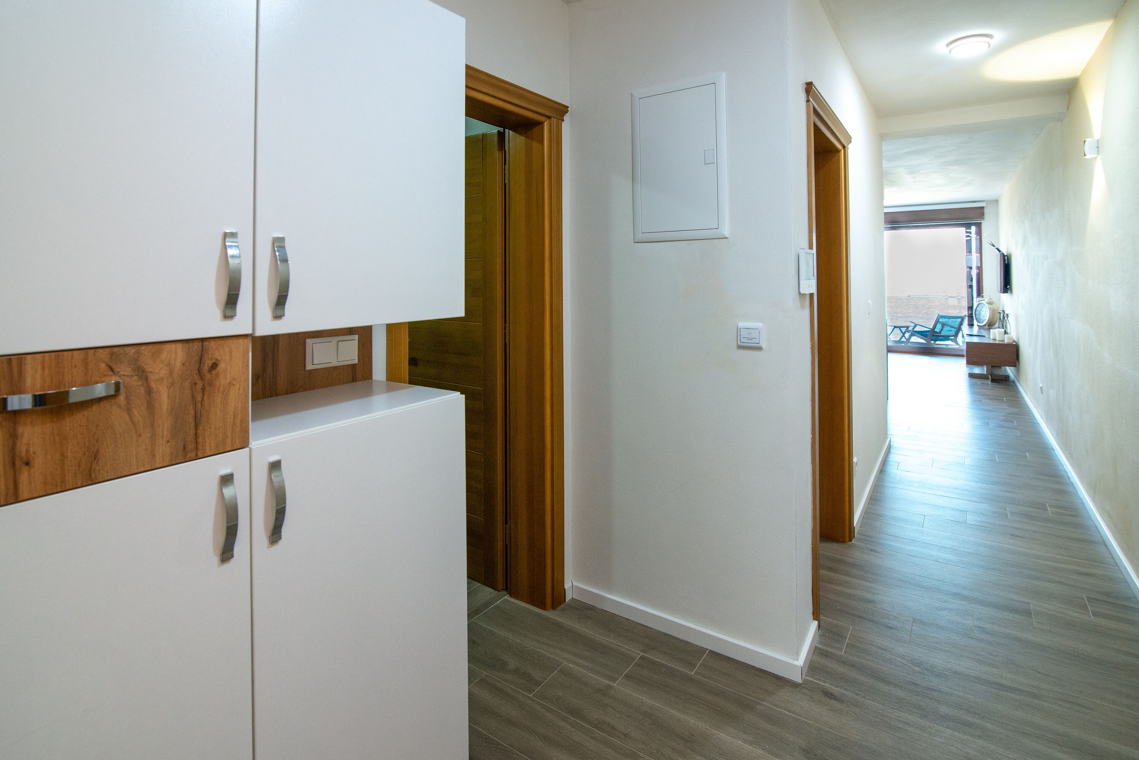 A hallway with white cabinets, a wooden door, and a view to a balcony.