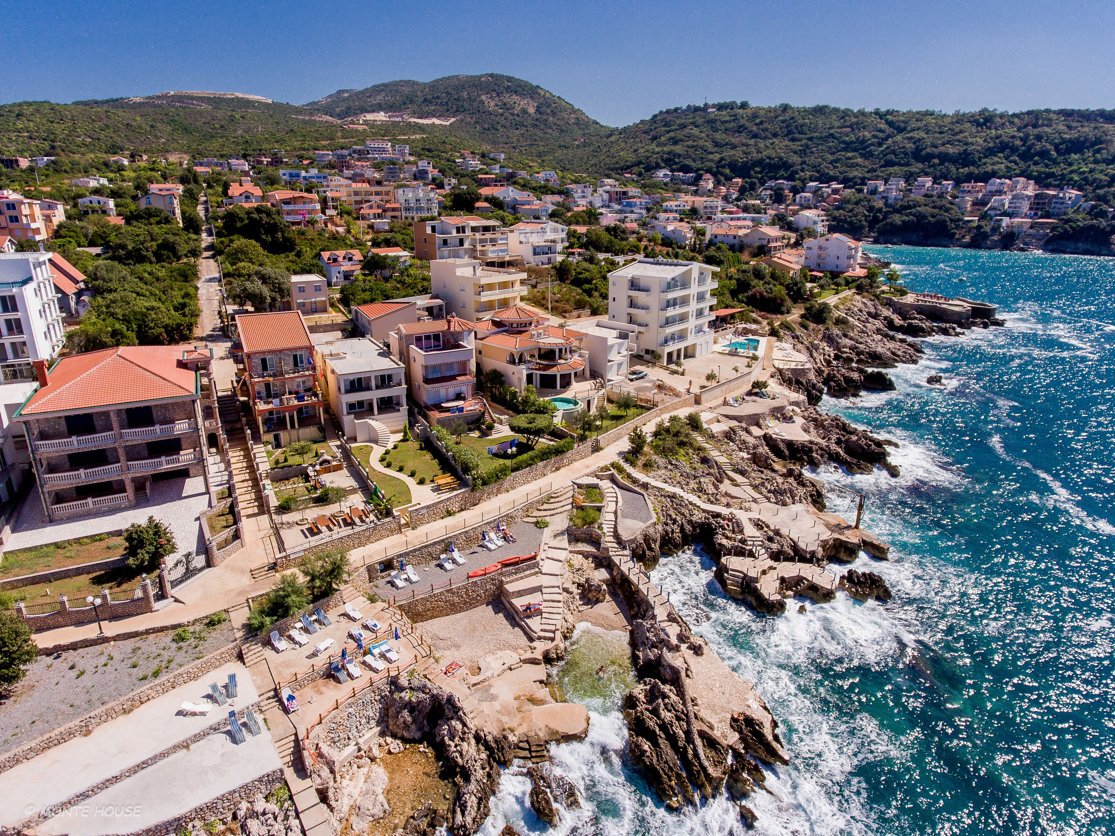 Un pueblo costero con un litoral rocoso, edificios con balcones y una vista despejada del mar.