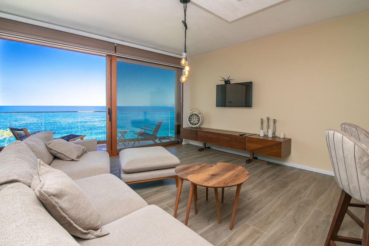 A modern living room with a large sliding glass door leading to a balcony with a view of the sea.