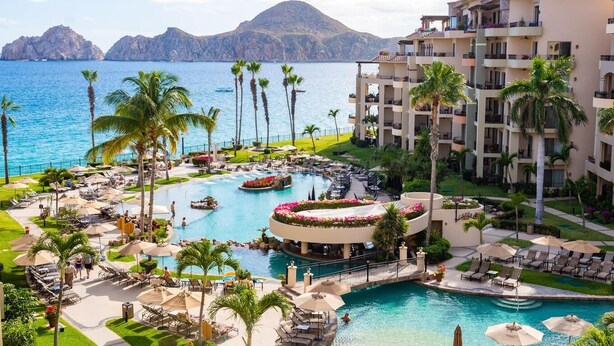 Un resort con una piscina grande, palmeras y vista al mar.