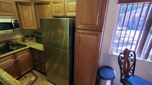 Una cocina con armarios de madera, un refrigerador de acero inoxidable, un microondas y una ventana con barrotes.