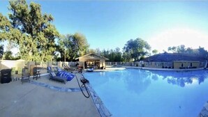 Piscina con sillas de descanso y un pequeño edificio, rodeado de árboles.