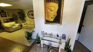 Un área de recepción con una estatua de Buda, dos sofás, una mesa de vidrio y plantas en macetas.