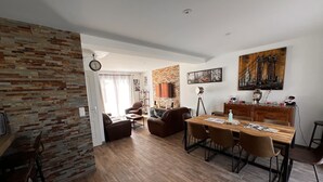 A spacious living area with a wooden dining table, leather sofas, and a brick accent wall. - Maison Chaleureuse Tout Confort (Amboise)