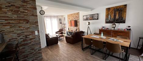 Amplia sala de estar con una mesa de comedor de madera, sofás de cuero y una pared de ladrillo decorativa.
