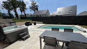 A backyard with a hot tub, a pool, and a dining area with chairs and a table. - Maison Chaleureuse Tout Confort (Amboise)