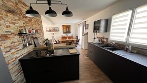A modern kitchen with a central island, wooden flooring, and a brick accent wall. - Maison Chaleureuse Tout Confort (Amboise)