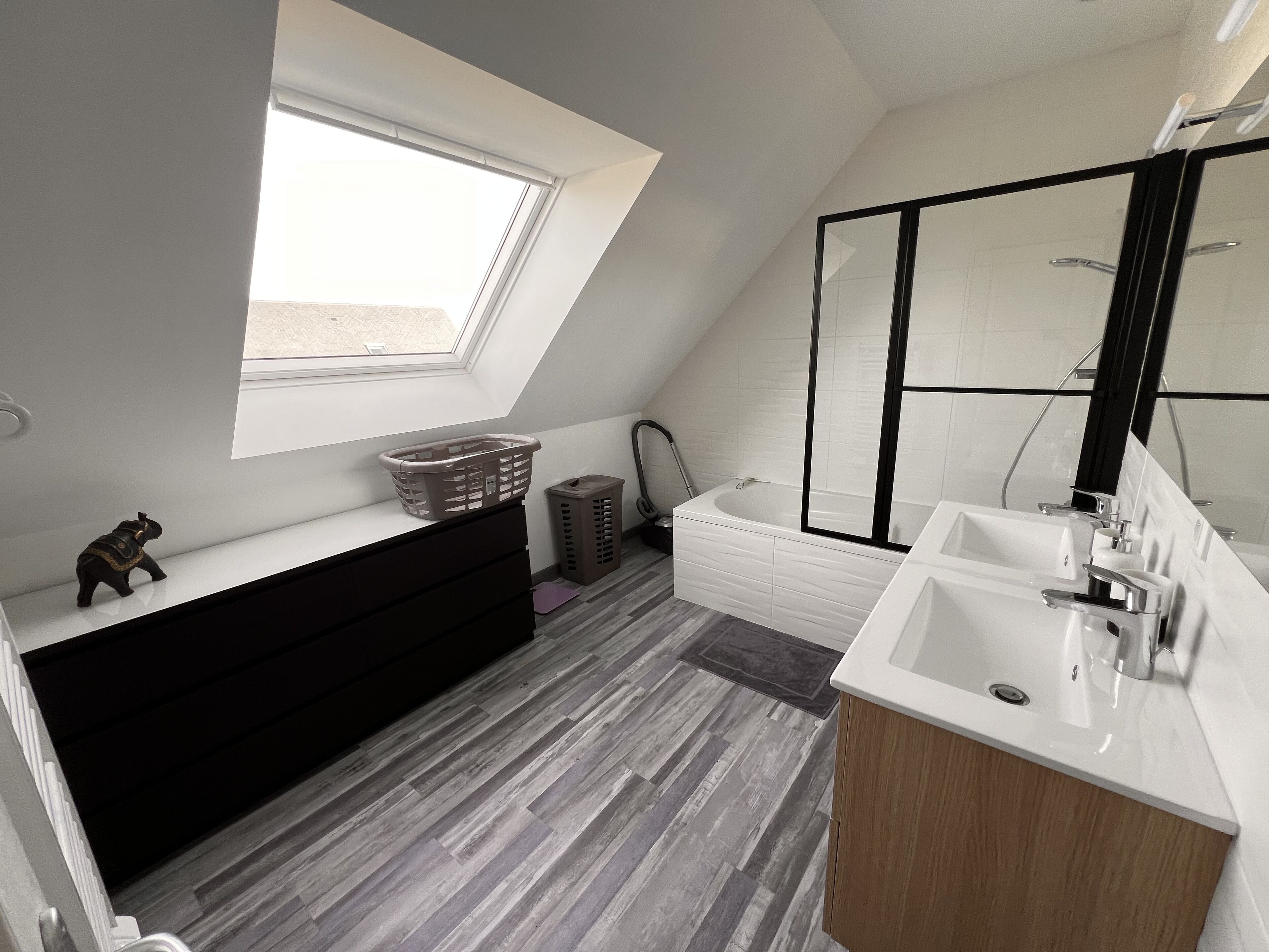 A modern bathroom with a skylight, a bathtub, a large mirror, and a wooden vanity.