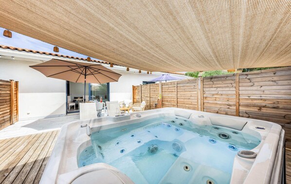 A hot tub area with a wooden deck, outdoor furniture, and a pergola providing shade.