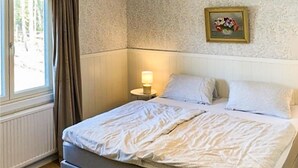 Une chambre à coucher avec un lit, une lampe de chevet, une fenêtre avec des rideaux et un tableau accroché au mur.