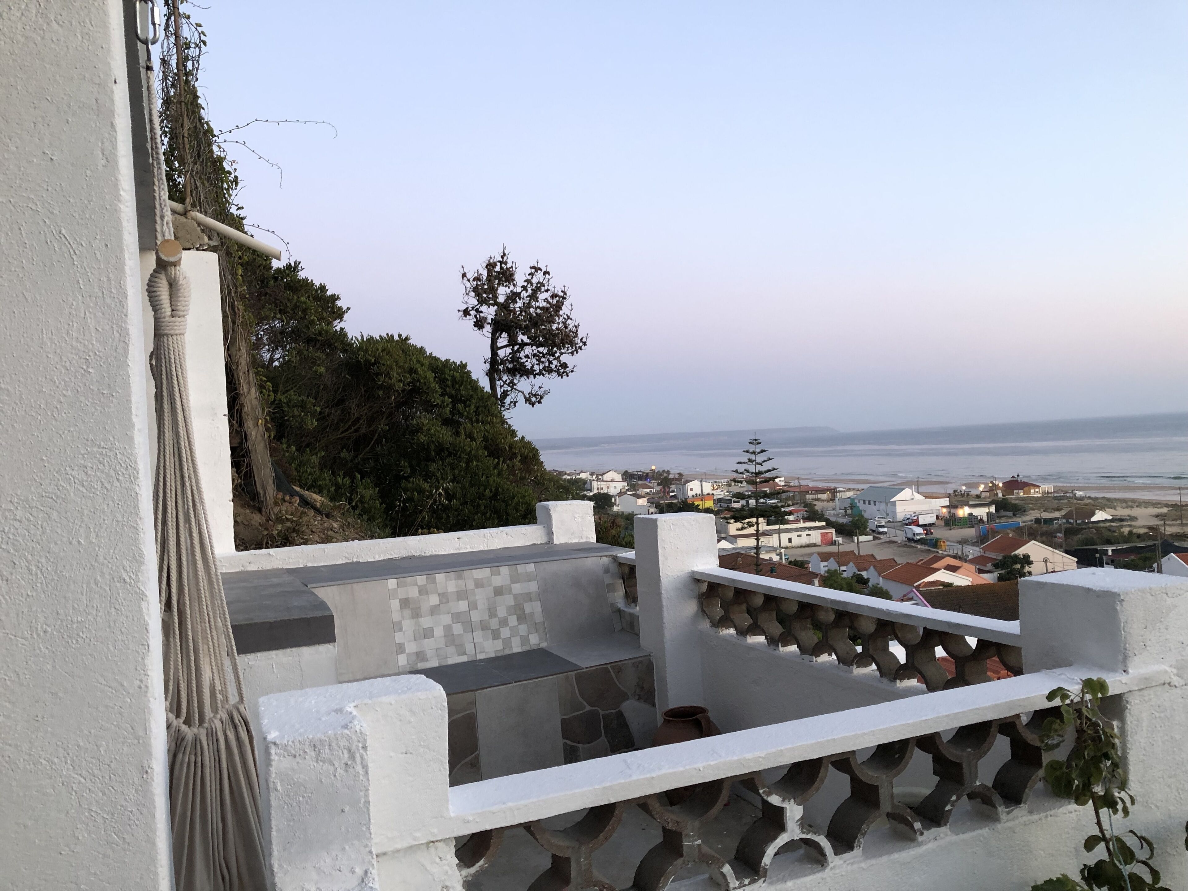 Una terraza con vista a un pueblo costero, una pared blanca y un macramé colgante.